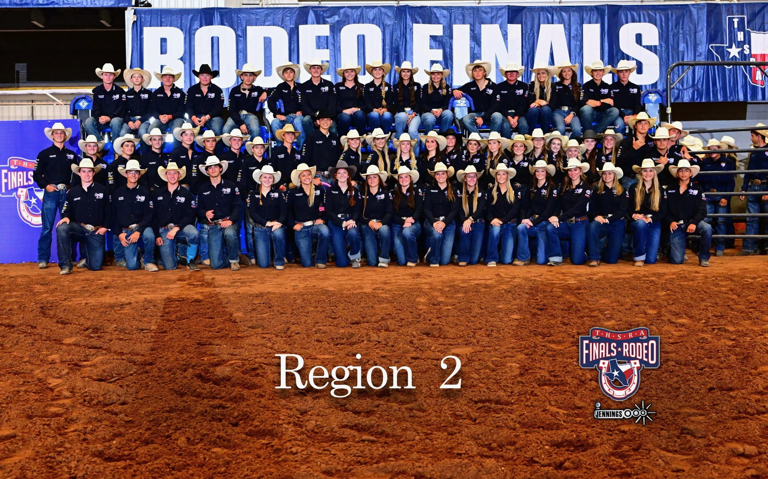 A group of young rodeo participants wearing cowboy hats and western shirts, posing together for a group photo in front of a blue banner with the words 'BODEFENAS' and symbols related to rodeo in an indoor arena.