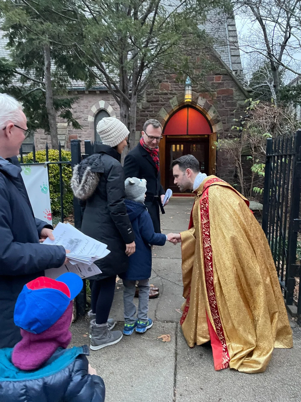 Rev. Ben DeHart, in a gold cope, greeting families at the red door of St. John's on Christmas Eve
