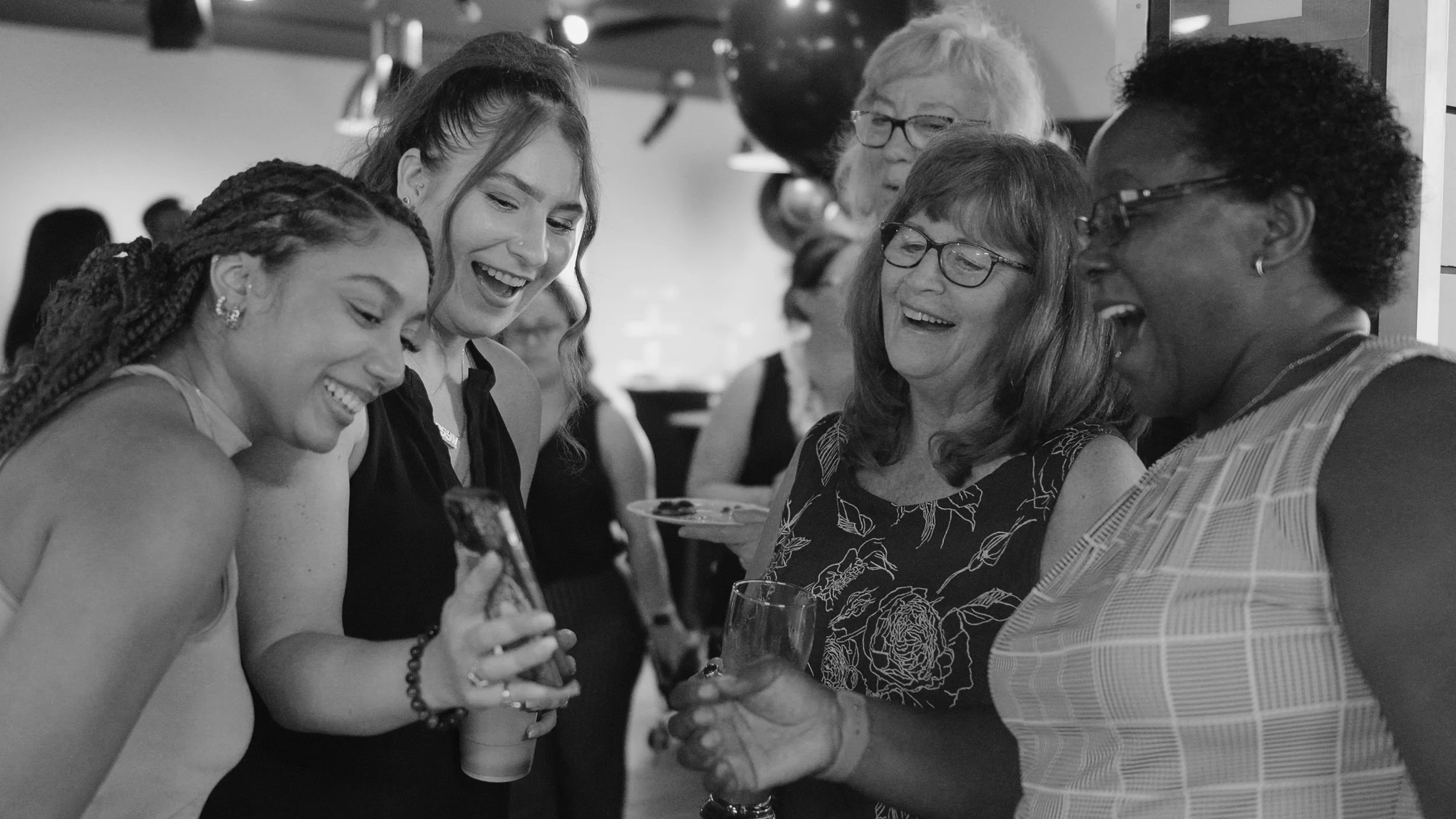 Group of women smiling and looking at a smartphone at a social event.