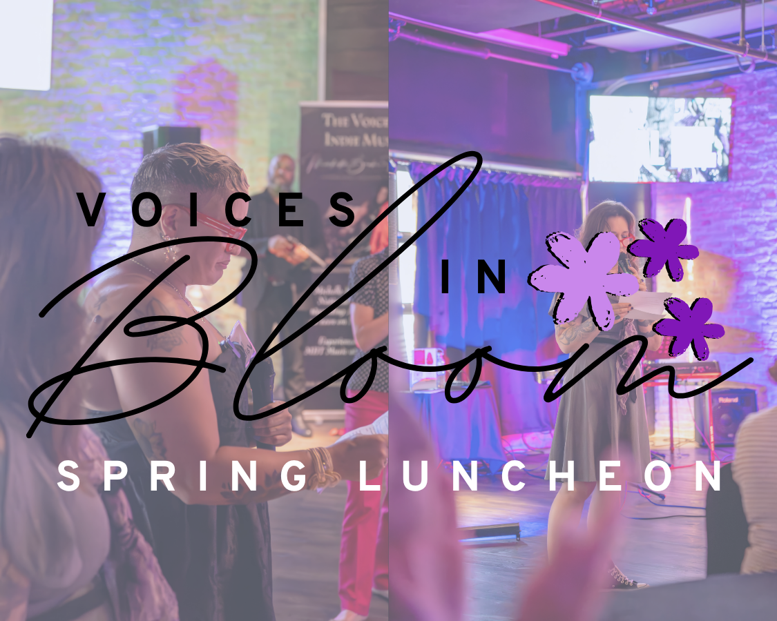 A woman with tattoos and glasses speaking at a conference or luncheon, with an audience seated in front of her. The background has exposed brick walls and purple lighting, giving a vibrant atmosphere.