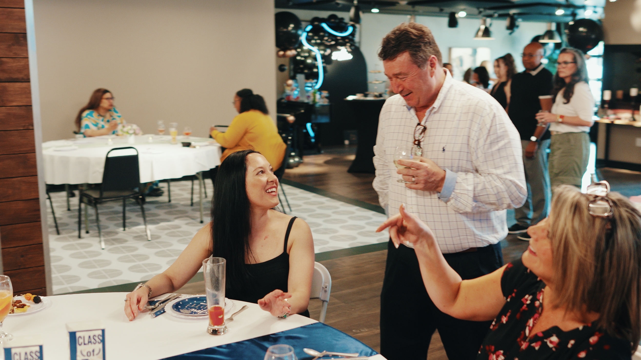 People socializing at an indoor event with tables and decorations.