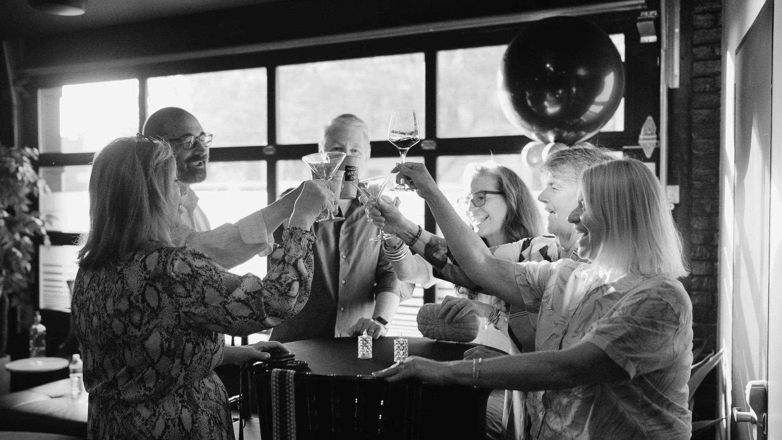 Group of smiling adults toasting with drinks in a social gathering.