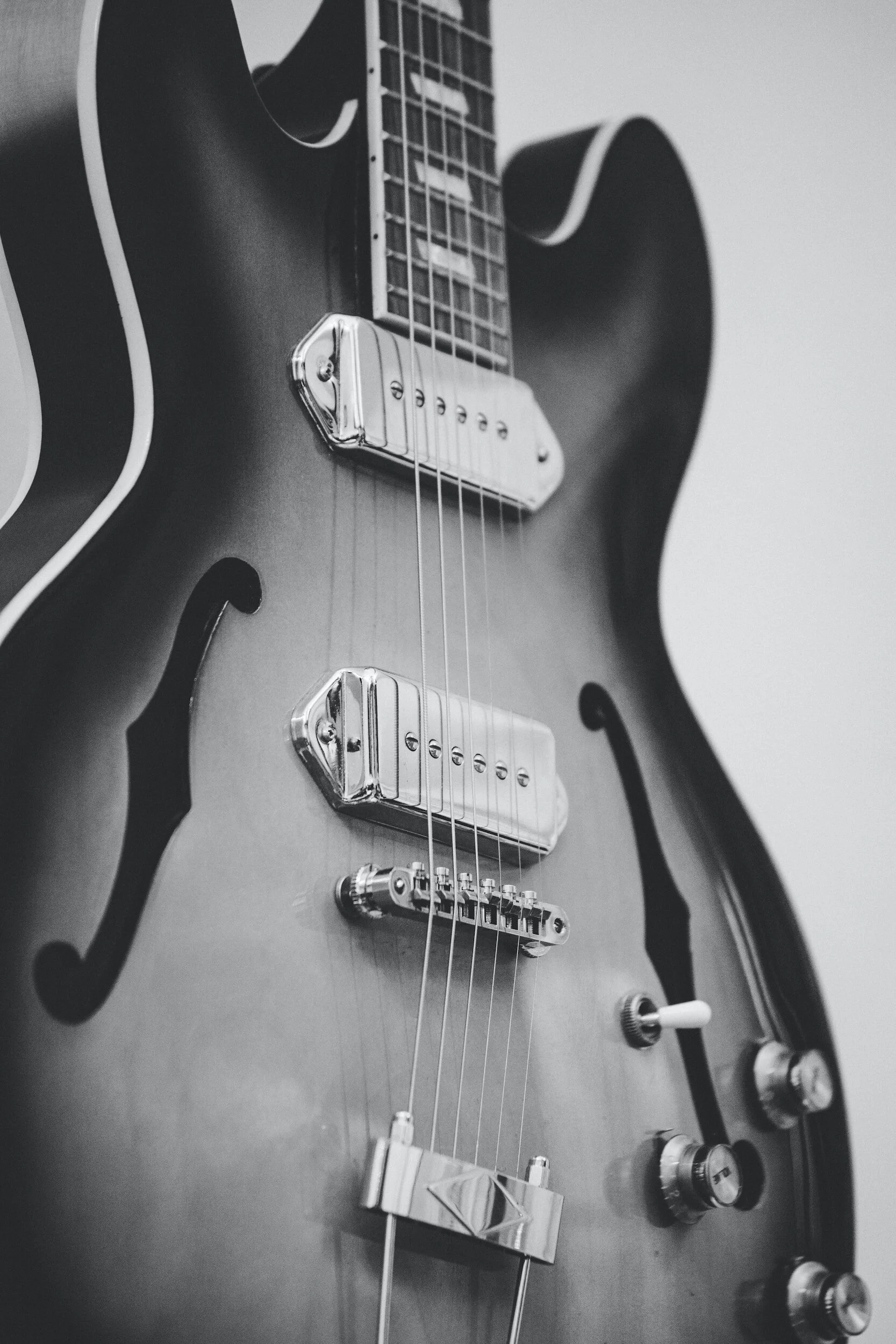 Black and white photo of an electric guitar showing the body, pickups, bridge, and part of the neck with strings, knobs, and switches.