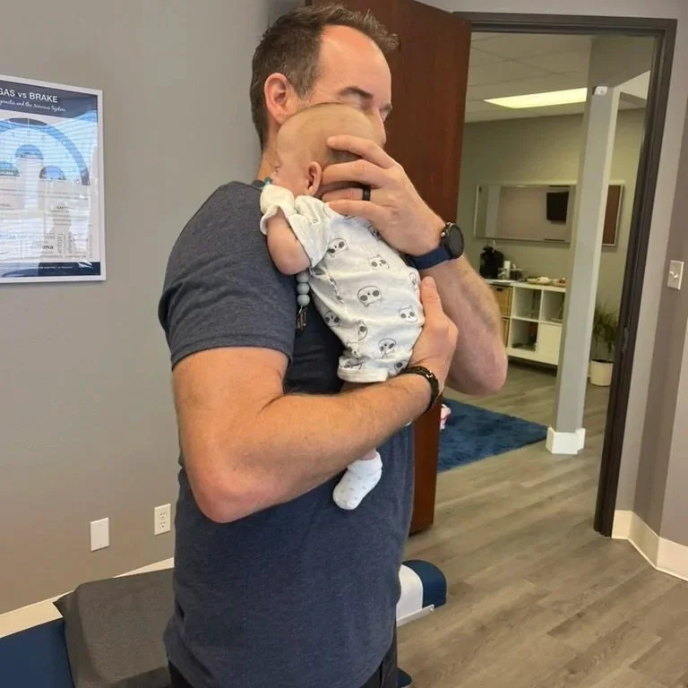 Pediatric chiropractor gently supporting an infant during a nervous system–focused adjustment