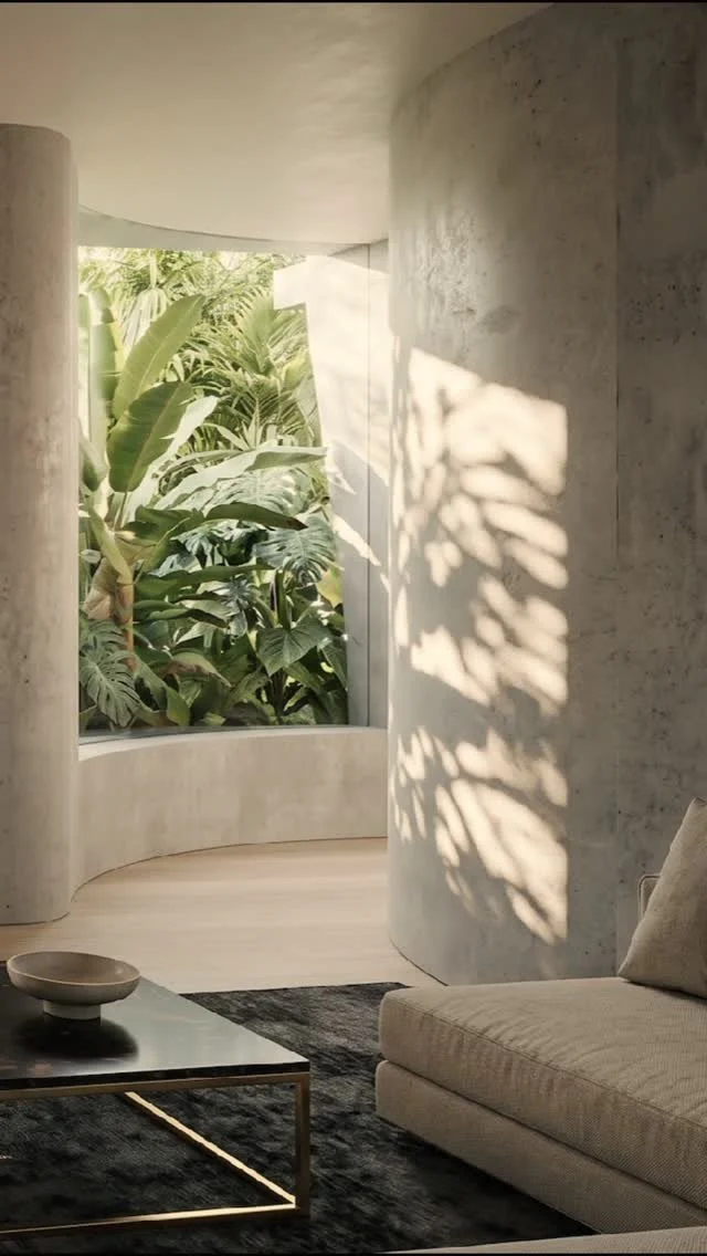 Living room with curved concrete wall, large window with tropical plants outside, black coffee table, beige sofa, and shadow of leaf pattern on the wall.