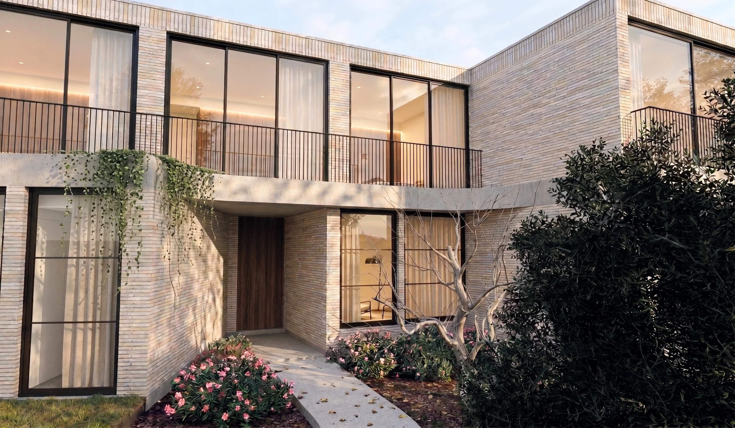 A modern two-story house with large glass windows, brick exterior, metal railing balcony, and landscaped garden with pink flowers.