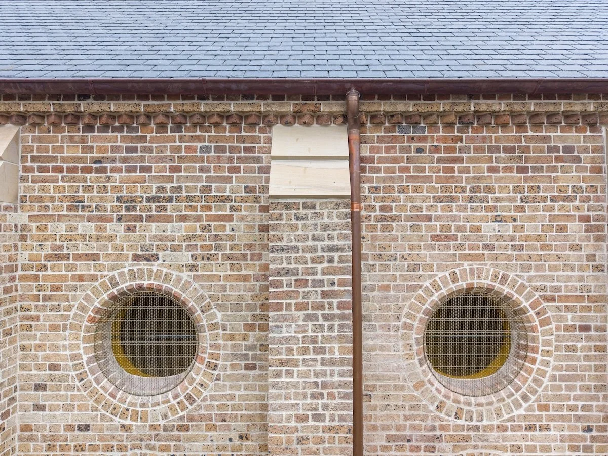 Brick building wall with two round windows and a brown drain pipe in the center.