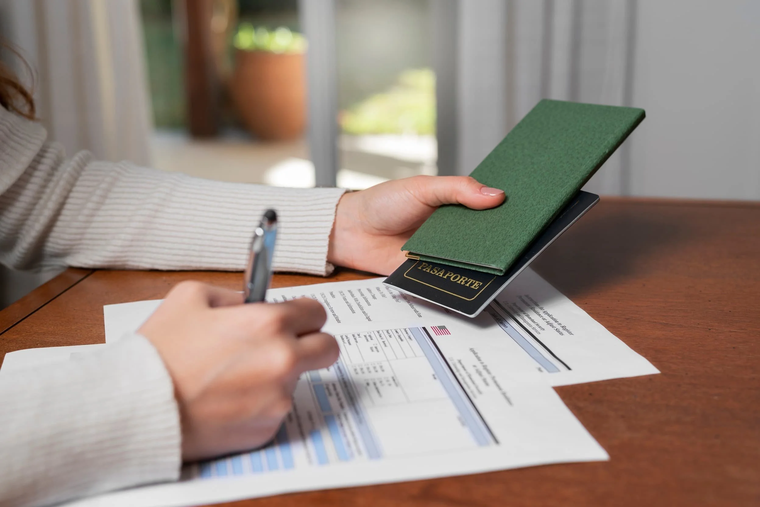 Close-up of a person holding a passport and filling out immigration forms at a wooden desk, symbolizing the EB5 visa application process under the RIA.