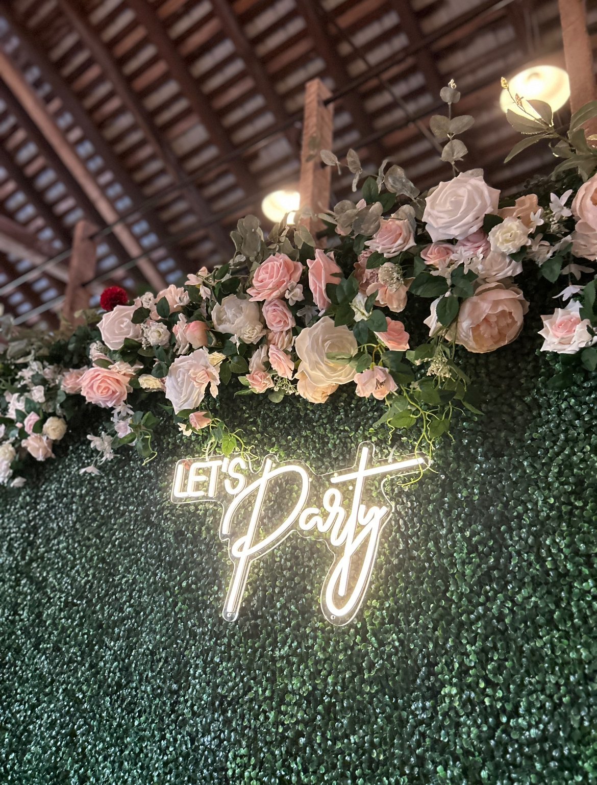 Boxwood greenery backdrop withrose floral garland and "Let's Party" neon sign