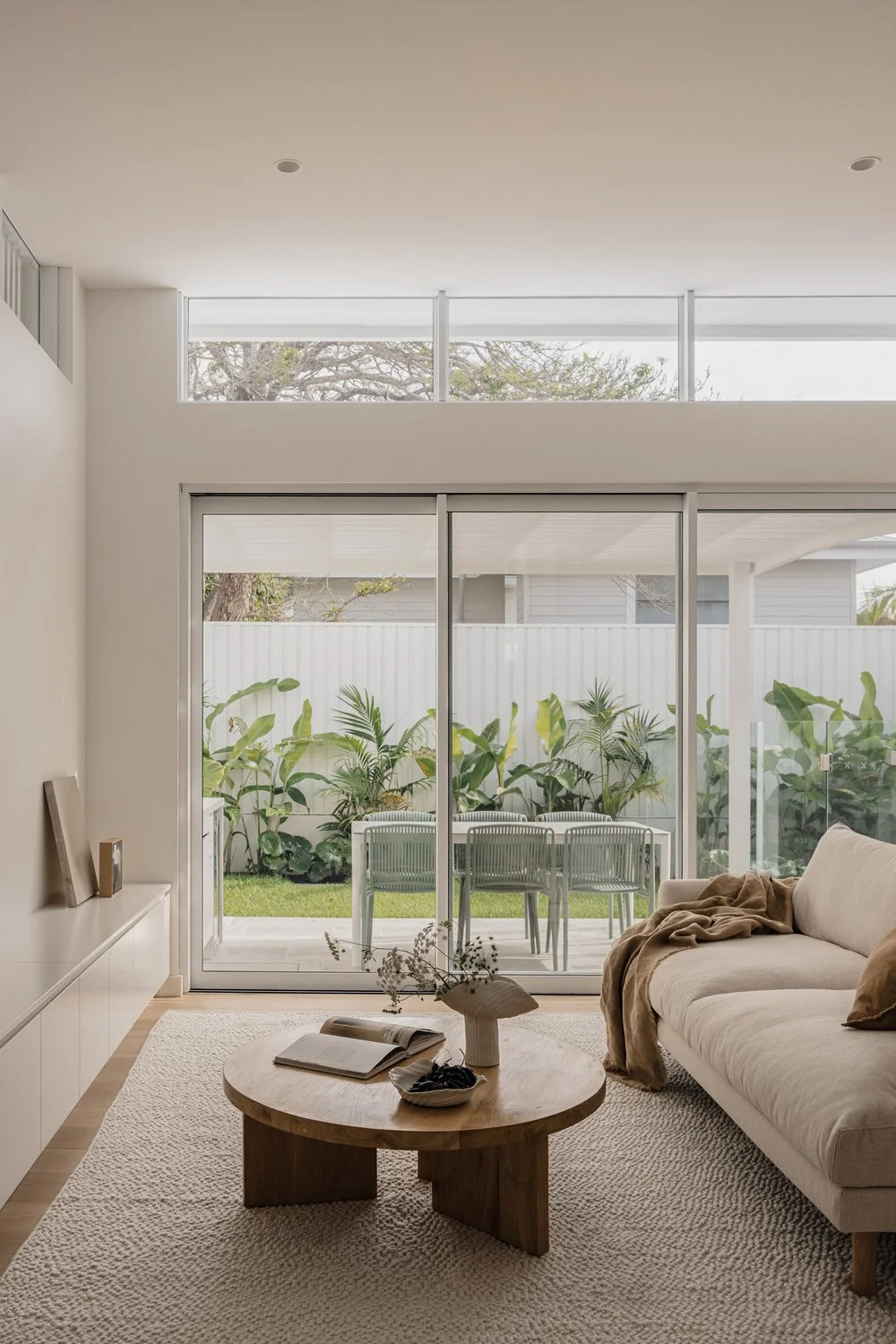 Living room with sliding glass doors opening to a patio with outdoor seating and lush greenery.