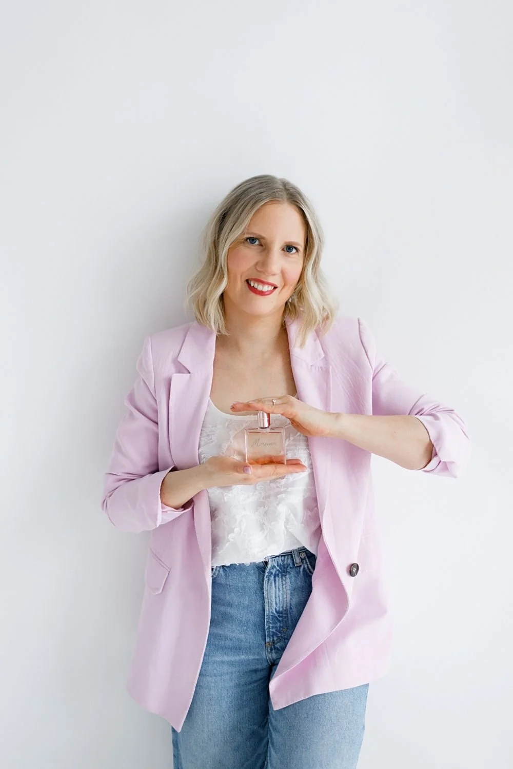 Nainen pitää kädessään kalligrafialla kaiverrettua hajuvesipulloa ja katsoo hymyillen kameraan.