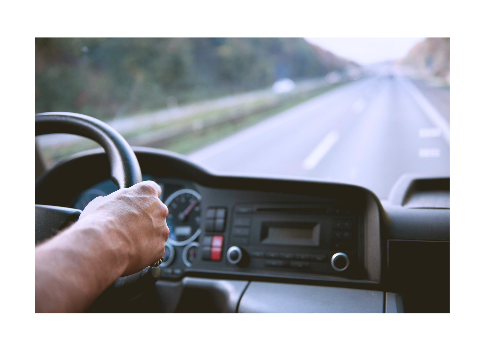 Fahrer hält Lenkrad eines Fahrzeugs, Blick auf die Straße, umgeben von Bäumen auf beiden Seiten.
