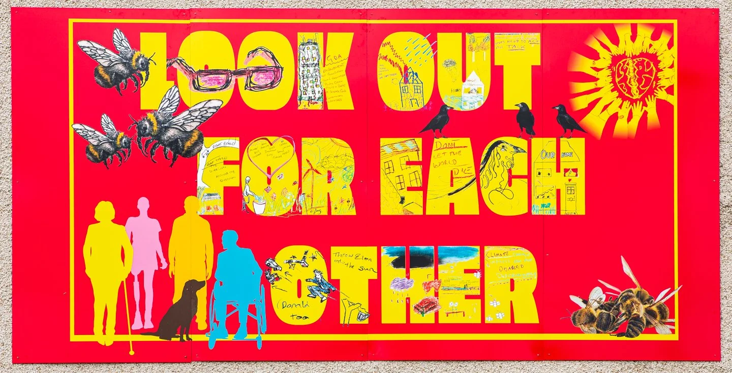 This photo shows a bright mural that is high on the outside wall of Greater Easterhouse Supporting Hands, with the text 'Look Out for Each Other' in yello, on a red background. Graphic elements include bees, glasses & silhouettes of disabled people
