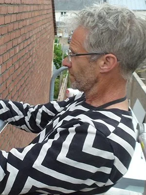 A side profile image of Andrew affixing a poster to a red brick wall.