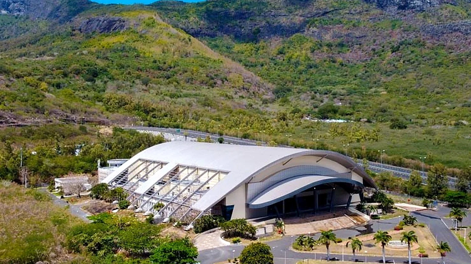 Elevated view of the completed convention centre and its distinctive long-span roof within the landscaped Pailles setting.