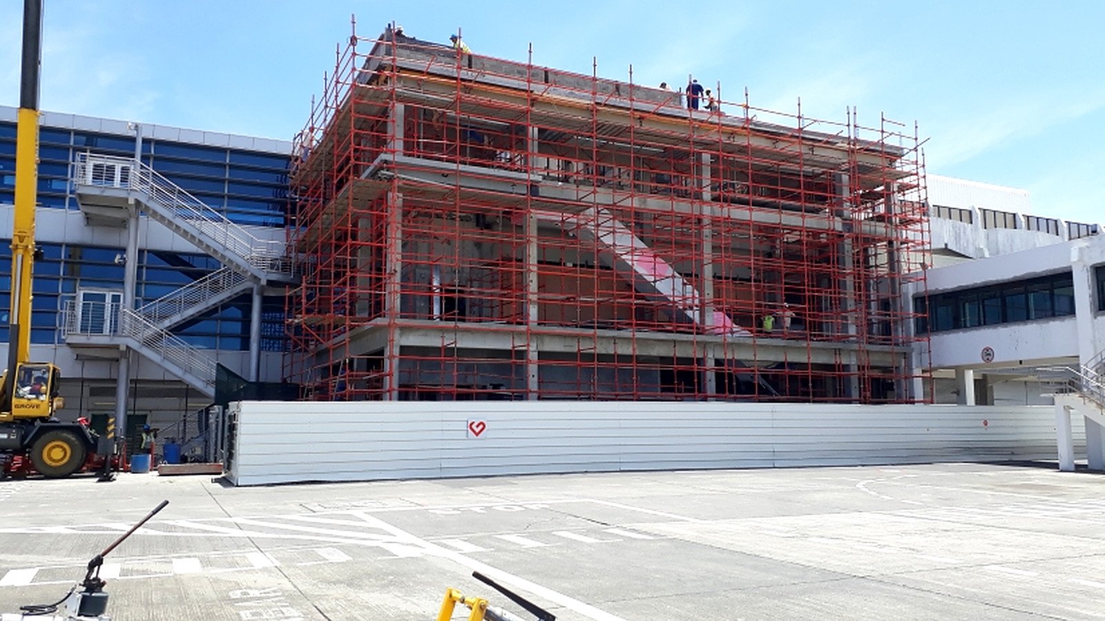 Wide airside view showing passenger boarding bridge works, apron controls and temporary logistics arrangements during the terminal refurbishment.