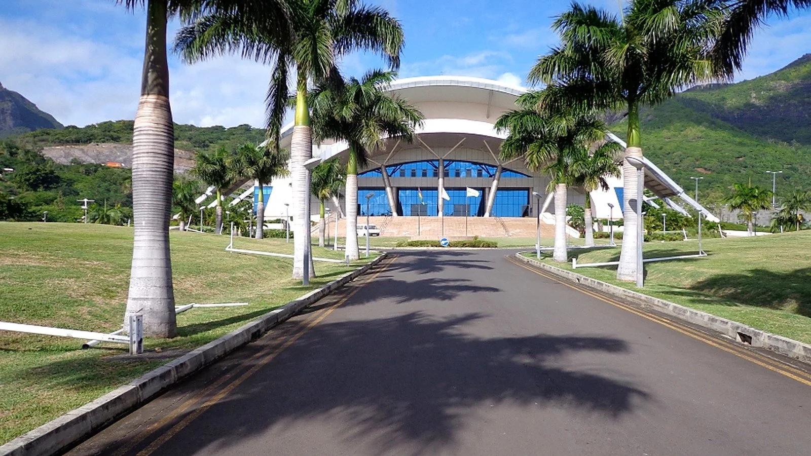 Front approach to the Swami Vivekananda International Convention Centre, showing its curved roof, glazed entrance, landscaped grounds and palm-lined access road.