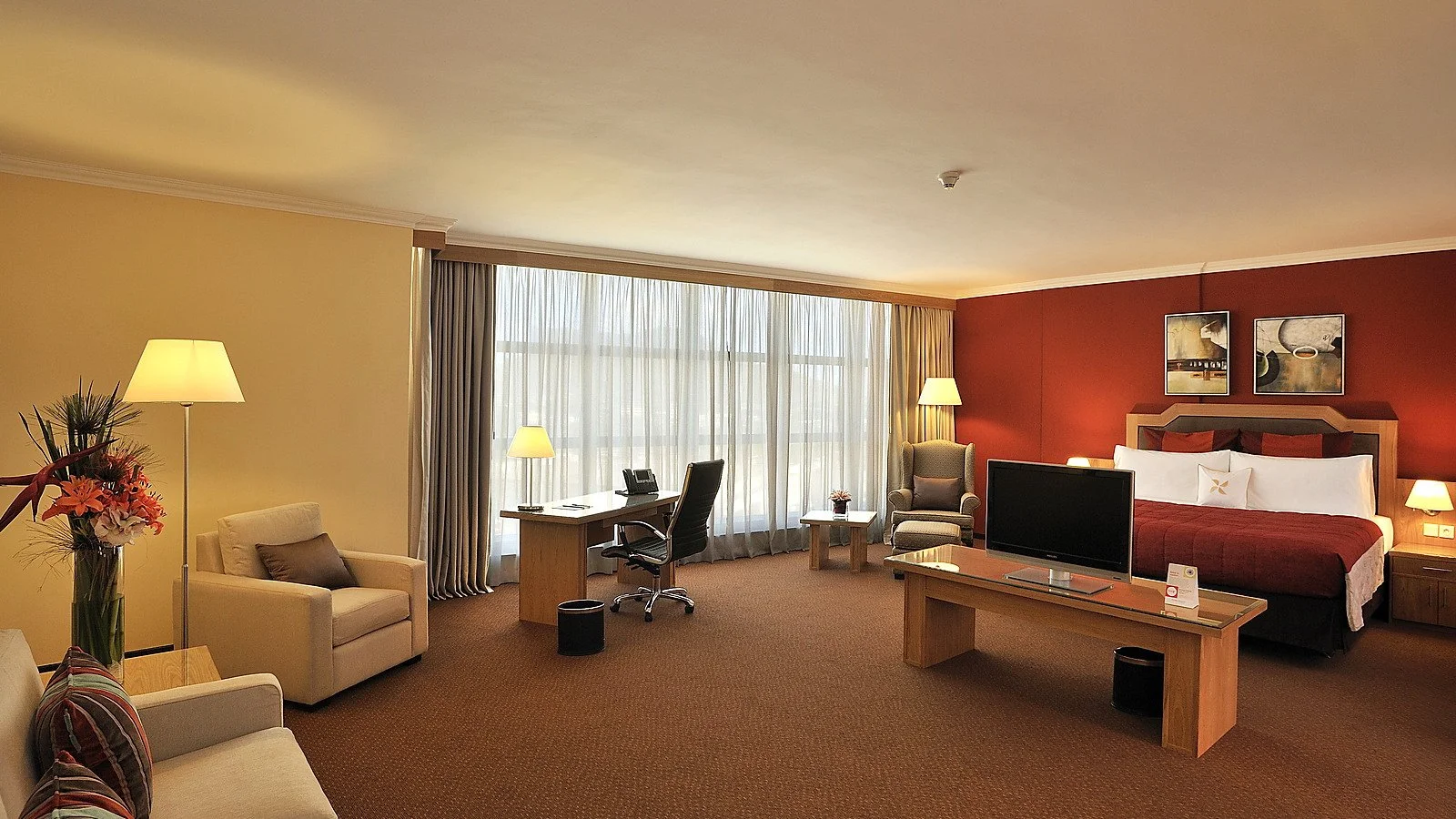 Completed hotel guest suite with sleeping, seating and work areas arranged beside a full-height window.