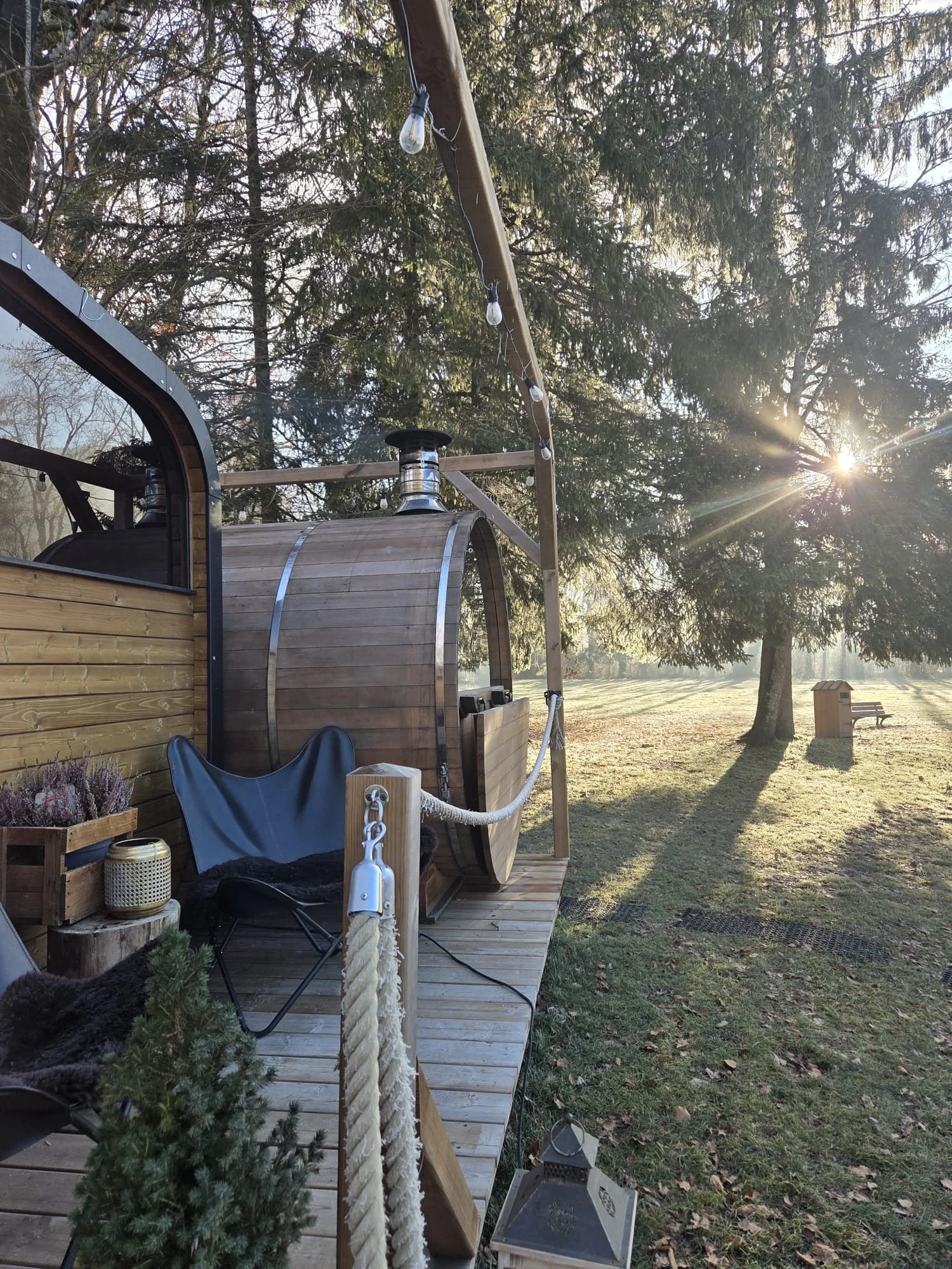Bastu74 barrel sauna on its wooden deck, with winter sun shining through the trees