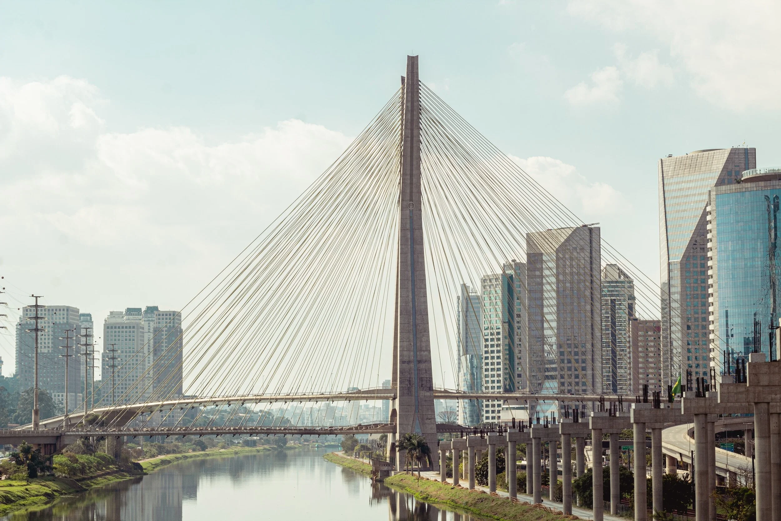 City skyline with a large cable-stayed bridge over a river, surrounded by modern skyscrapers, under a partly cloudy sky.