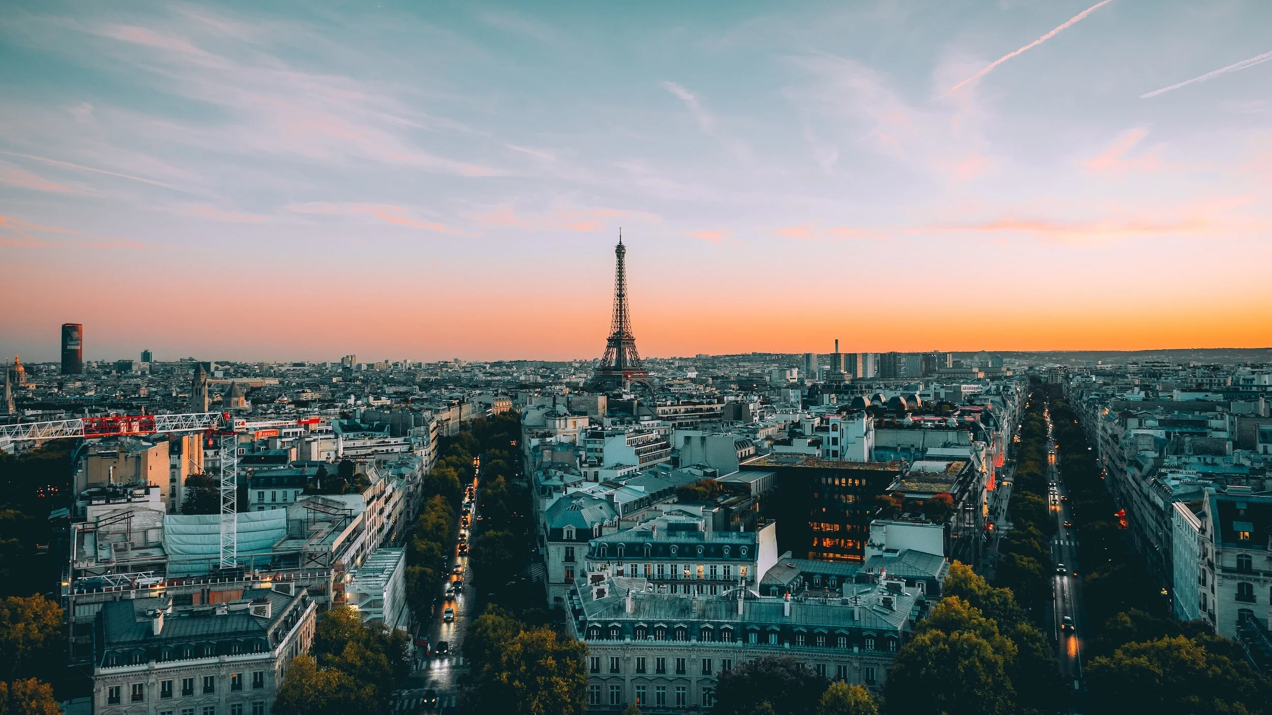 Cityscape of Paris with Eiffel Tower at sunset, showing buildings, streets, and a sky with wispy clouds and contrails.