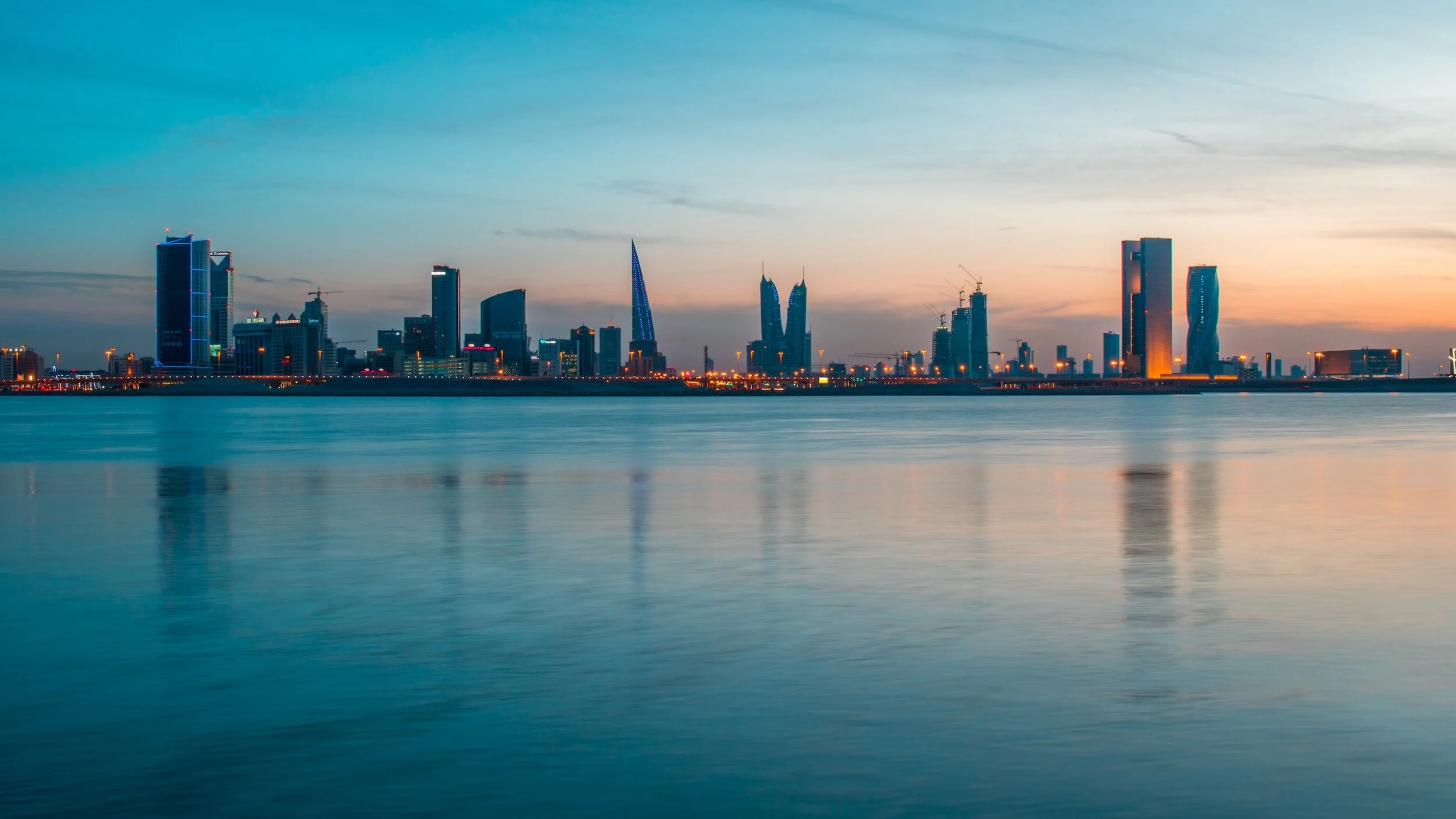 City skyline at dusk with modern skyscrapers reflected on calm water.