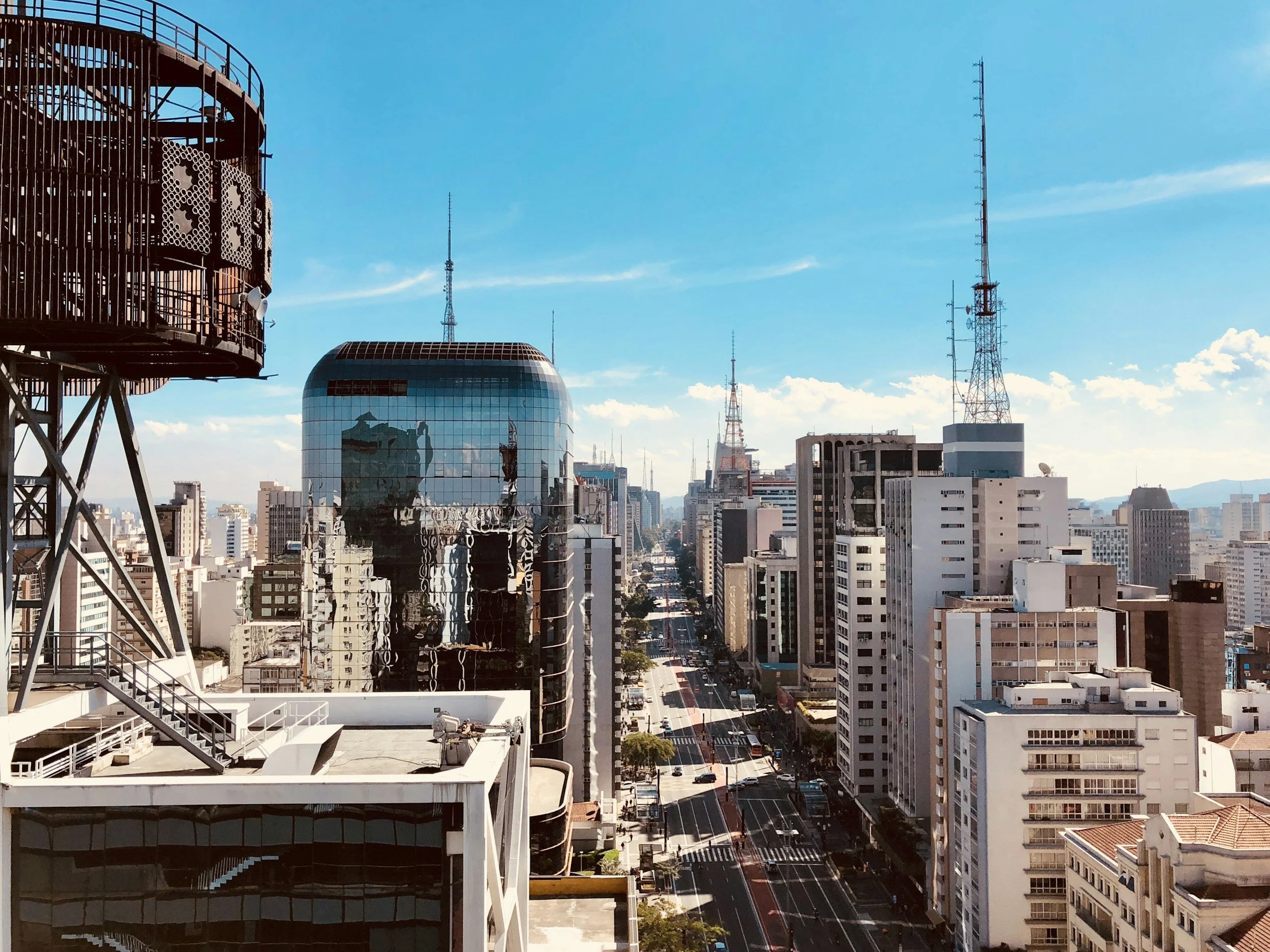City skyline with modern high-rise buildings, communication towers, and a clear blue sky.