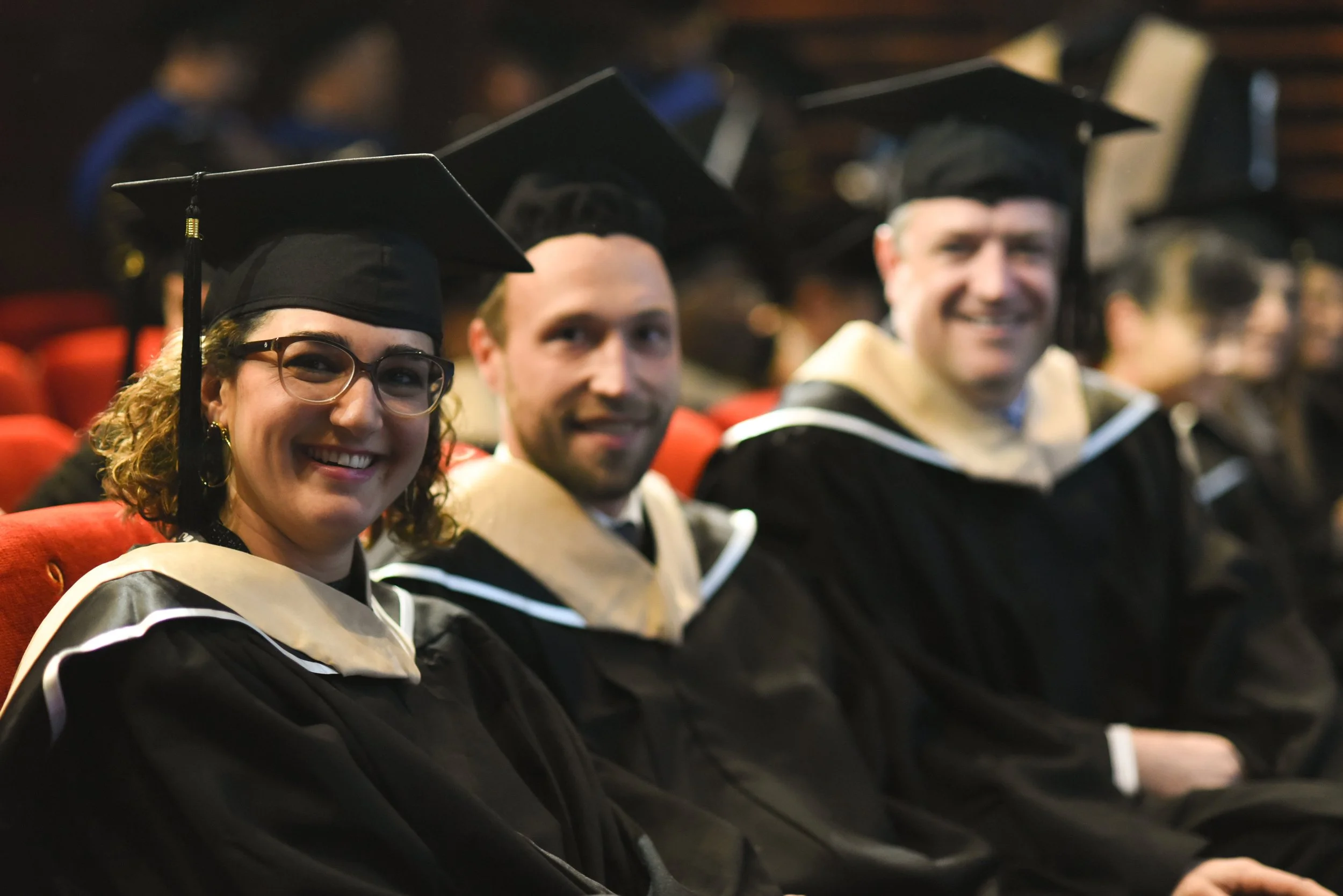 Graduates in caps and gowns sitting in an auditorium during a graduation ceremony.