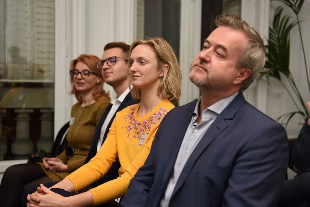 Four adults sitting attentively during a meeting or presentation in an indoor setting.