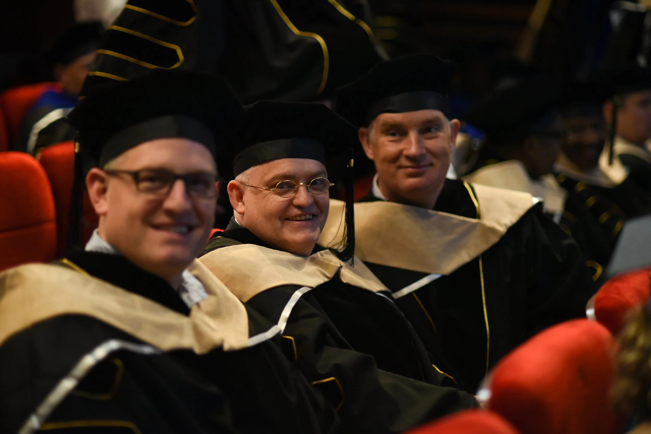 University graduation ceremony with graduates in caps and gowns seated in an auditorium.