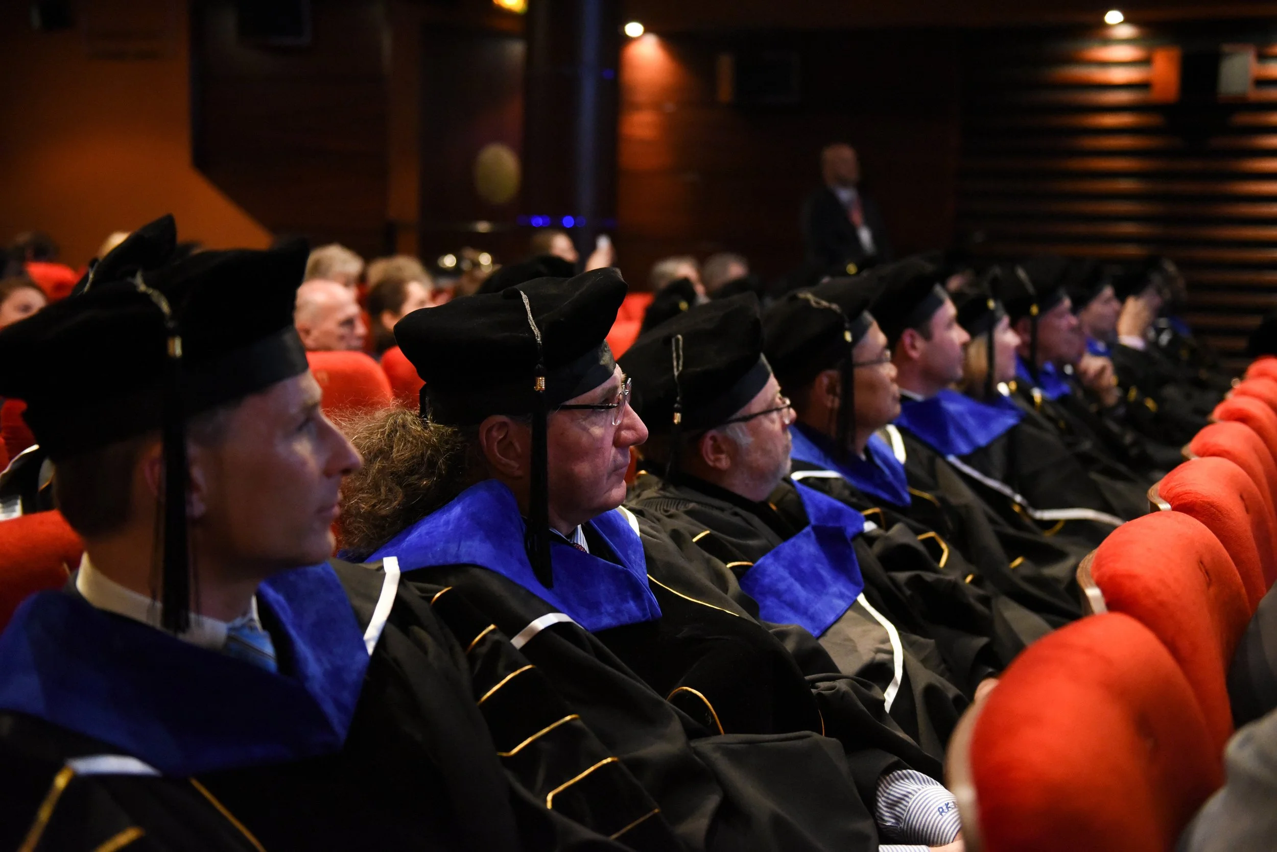 People in academic regalia seated in an auditorium during a graduation ceremony.