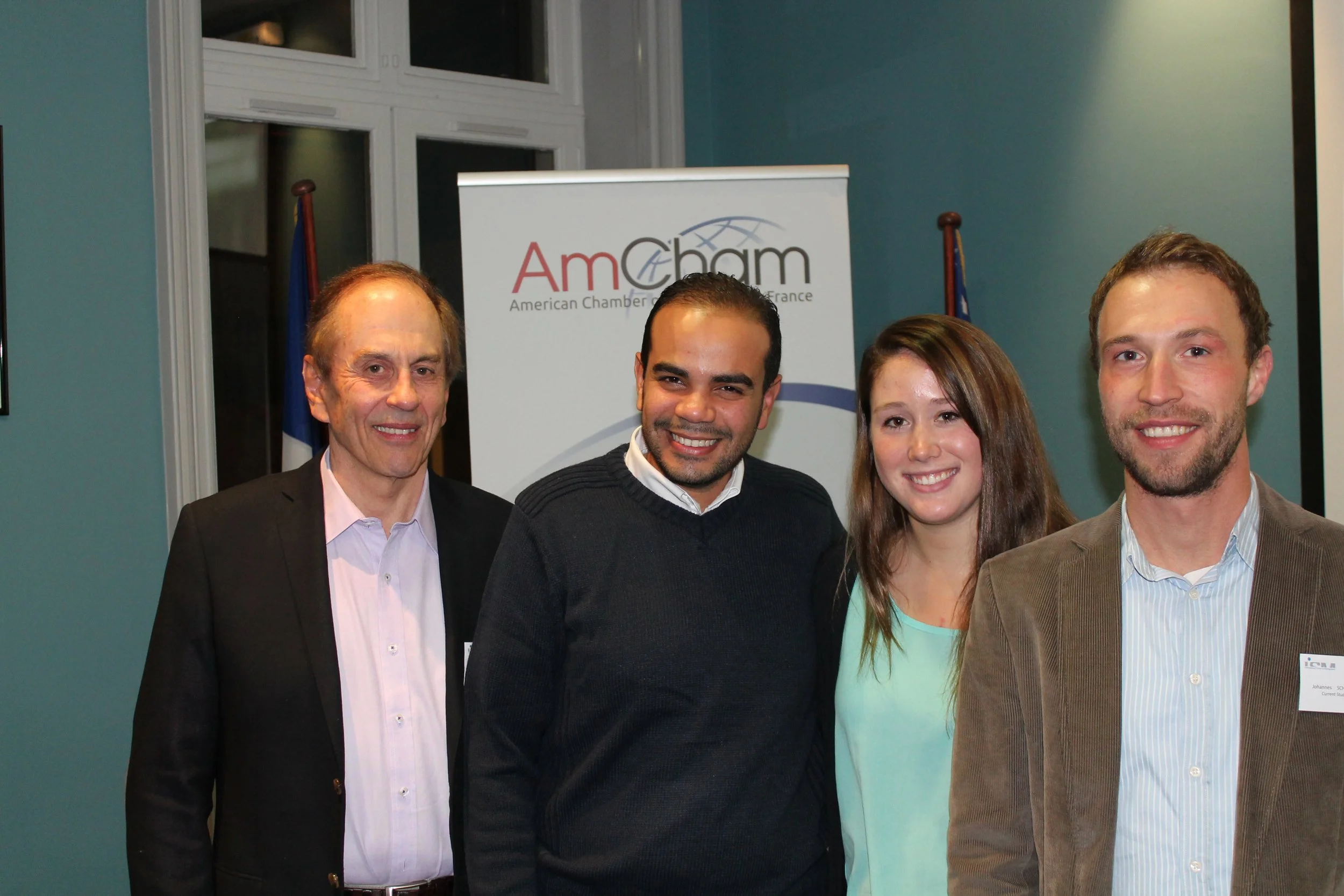 Four people smiling at an event, with a banner behind them reading 'AmCham' and 'American Chamber of Commerce in France'.