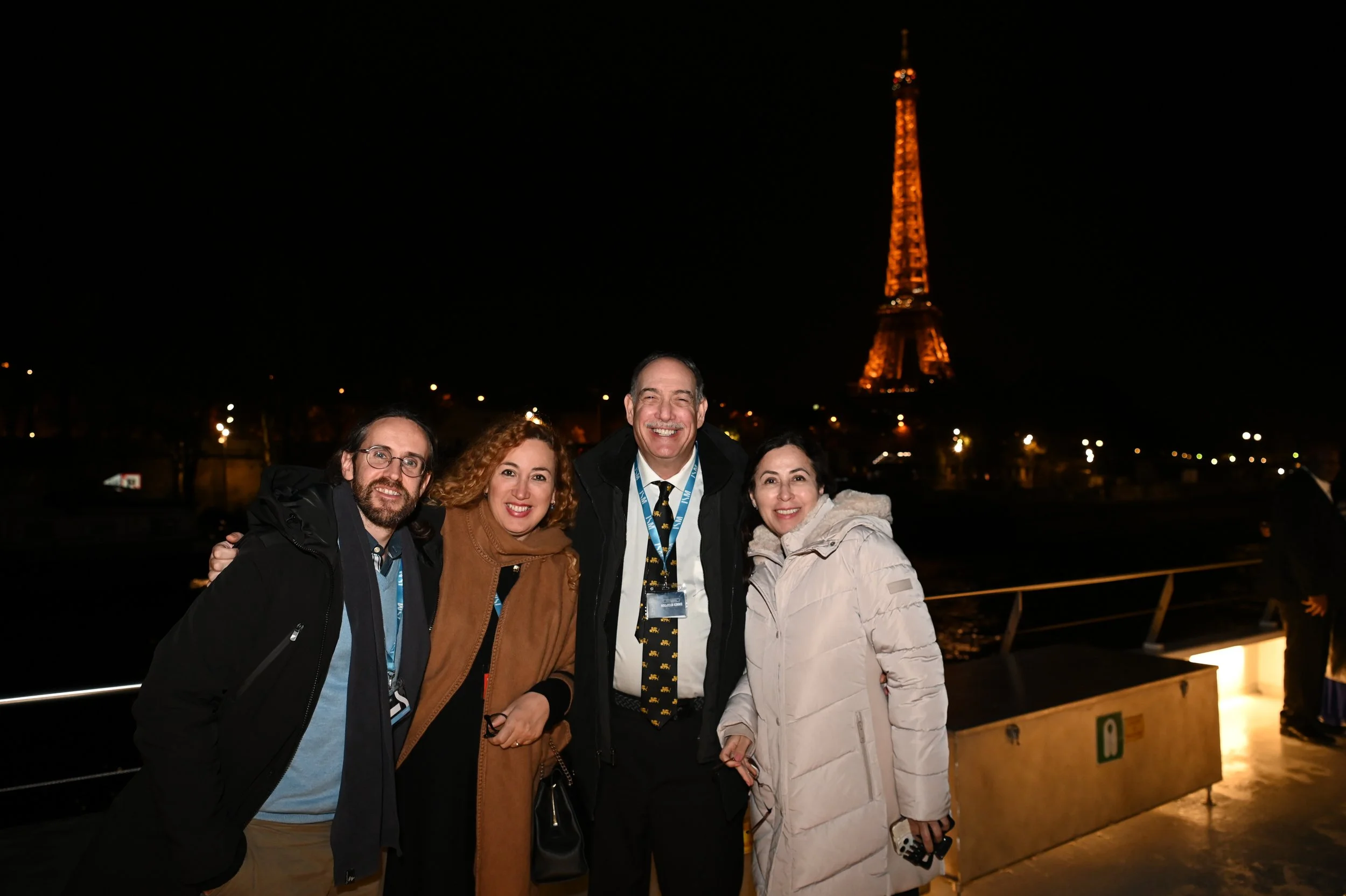 Four people smiling at night with the Eiffel Tower illuminated in the background.