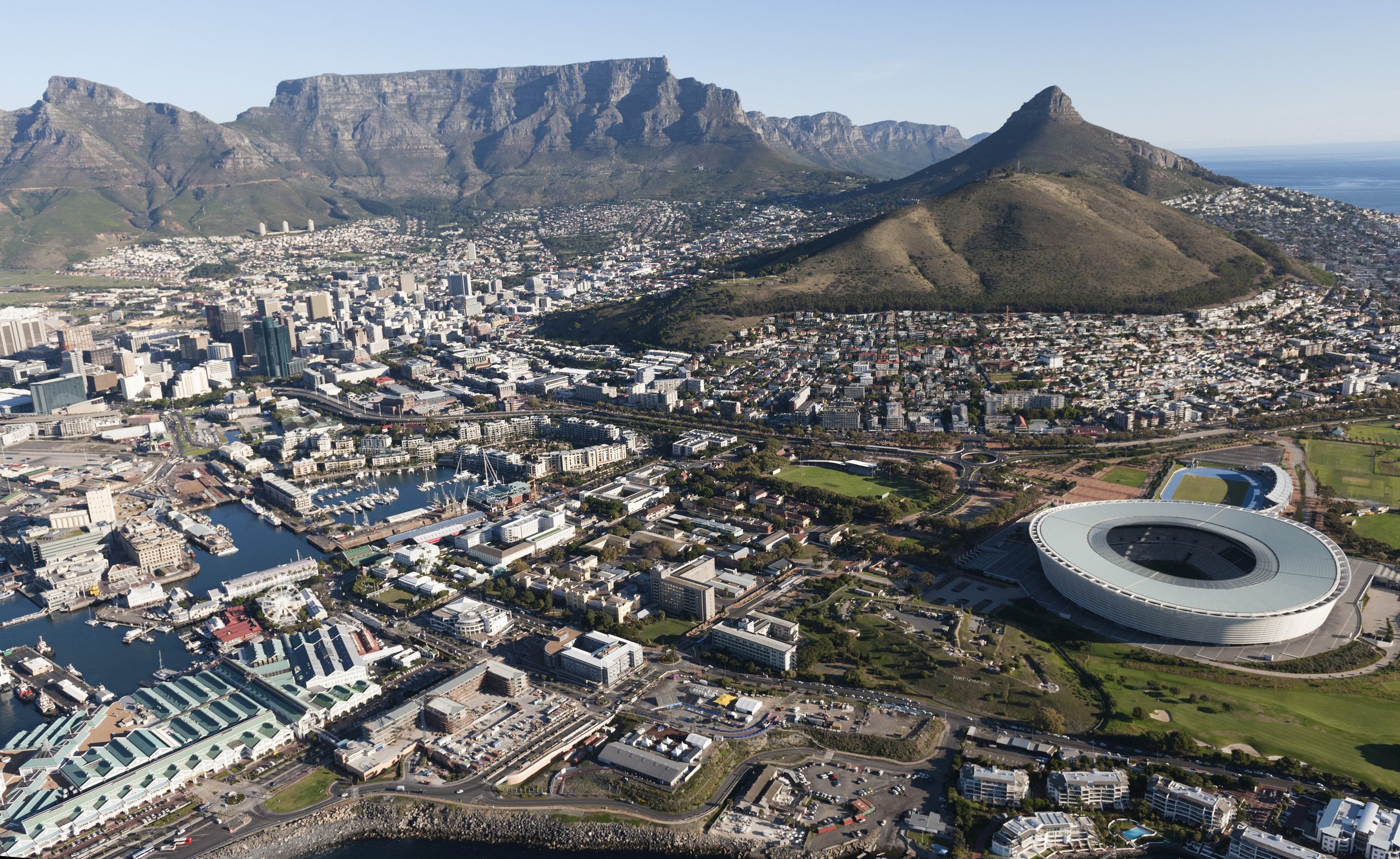 Aerial view of downtown Cape Town, South Africa, with Table Mountain in the background and the Cape Town Stadium in the foreground.
