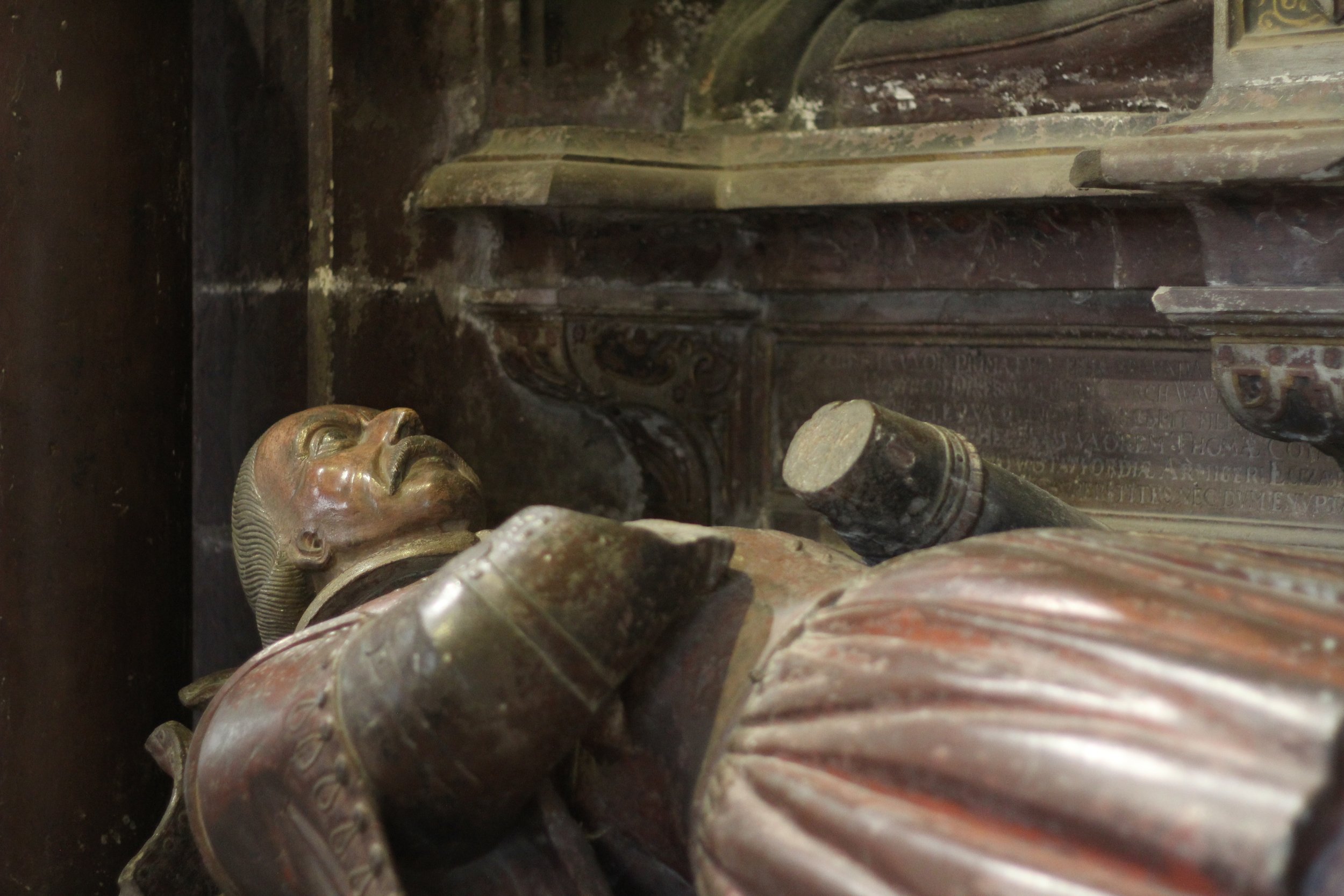 Close-up of a stone effigy in medieval armor resting on a tomb.