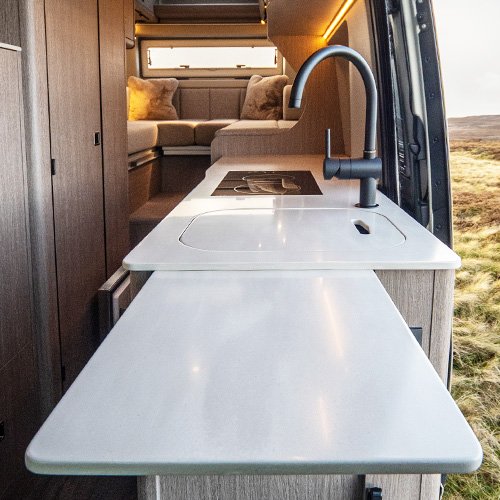 A beige countertop with a built-in sink and a chrome faucet, attached to a gray cabinet with a drawer, and a small extendable table or shelf on the side.