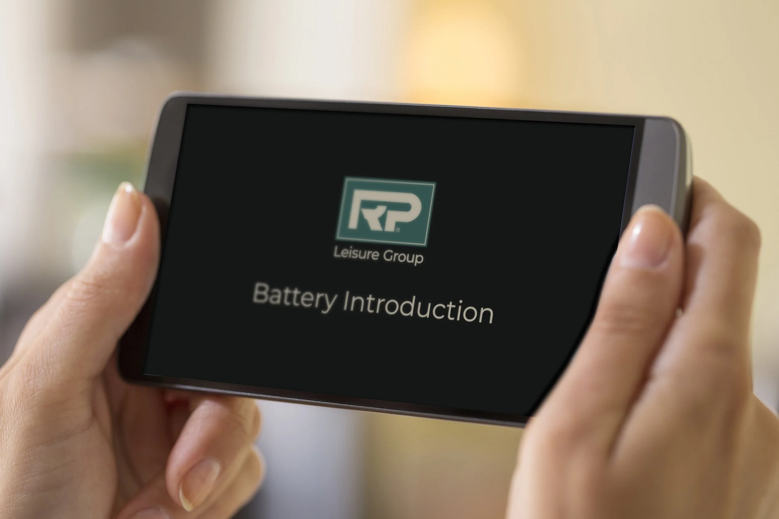 Person holding a smartphone showing a presentation slide with the logo and text for 'Leisure Group' and 'Battery Introduction'