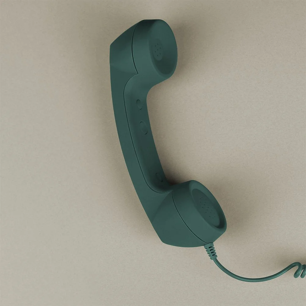 A teal-colored vintage telephone handset mounted on a beige wall with a coiled cord.