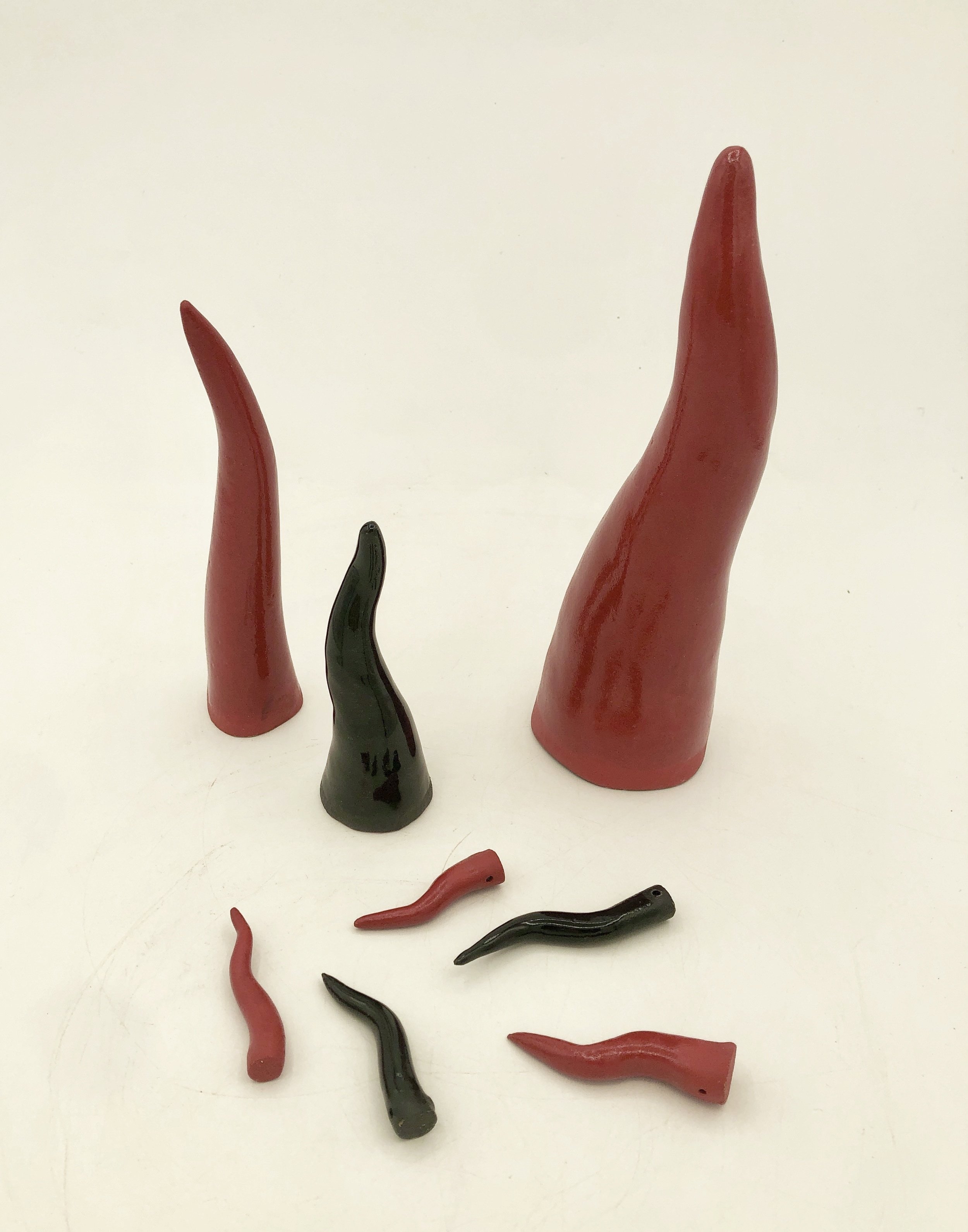 2 larger red cornicelli, a medium black cornicello standing upright, and 5 small red and black cornicelli scattered in front of them. Cornicelli are curved "horns".