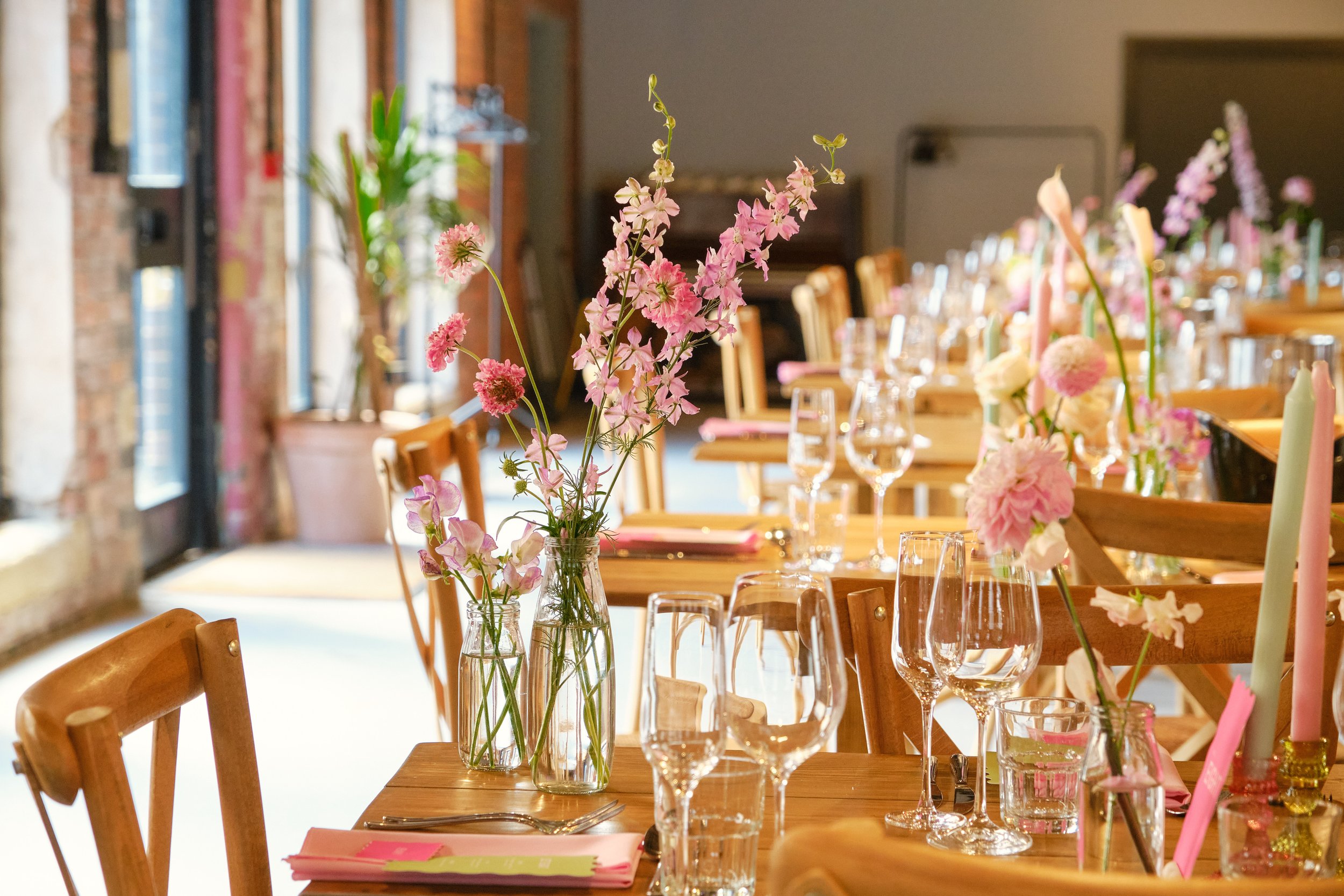 Wedding table arrangement at 'The Stables' decorated with brightly colored flowers, vases and candles on wooden tables.