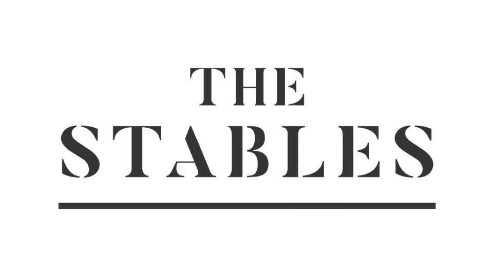 Black background with text that reads "The Stables" in large, bold, gray font, with a gray horizontal line beneath it.