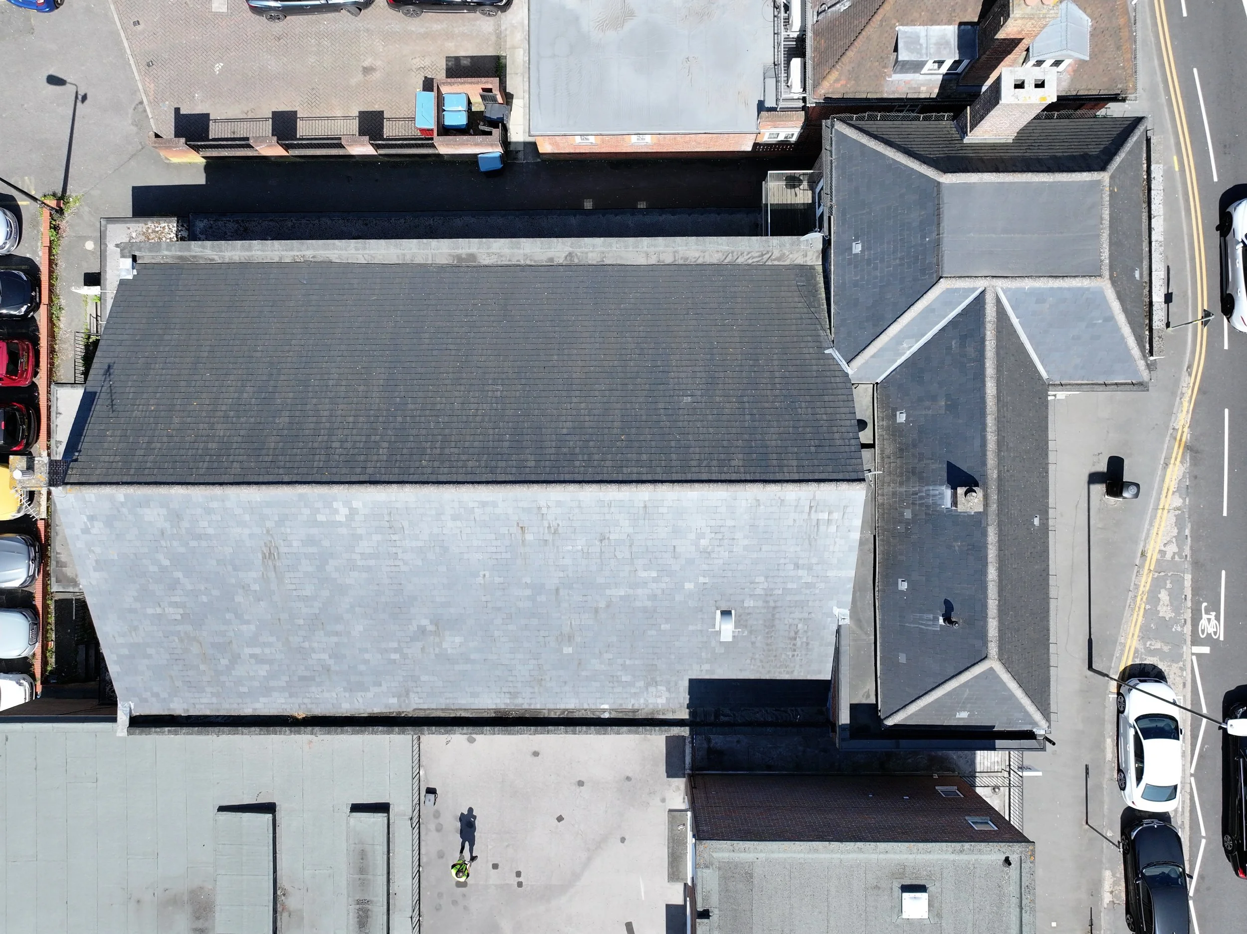 An aerial view of rooftops, with parts of a street showing parking cars, a bicycle lane, and a small alleyway.