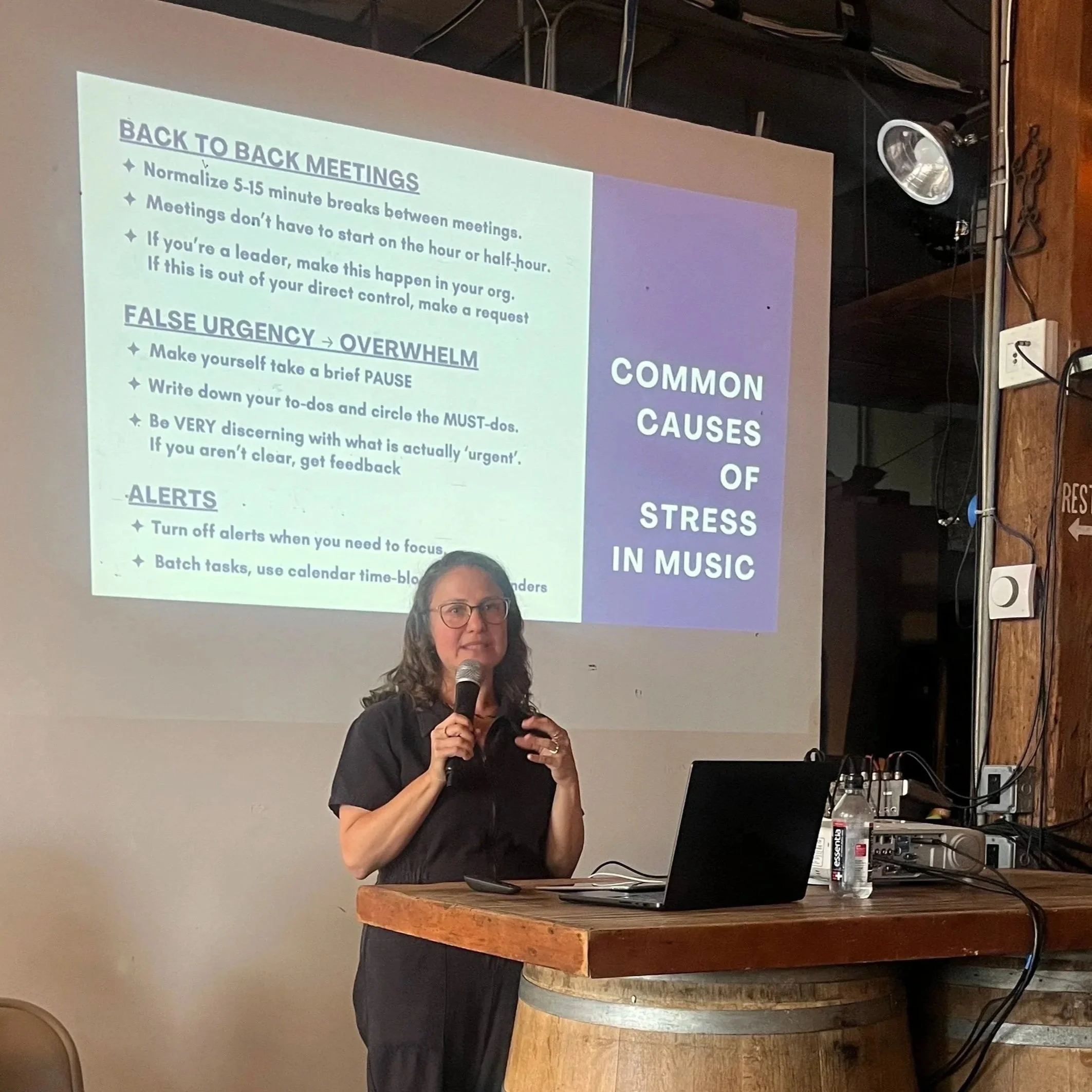 Nicole is speaking in front of a presentation slide at a conference. The slide contains tips about back-to-back meetings and handling stress.