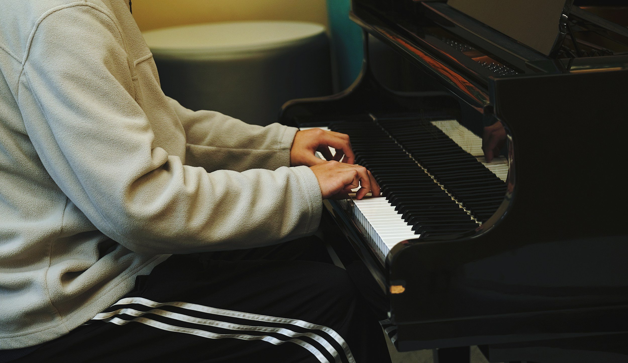 Person wearing a beige fleece pullover playing a black grand piano, focusing on their hands on the keyboard.
