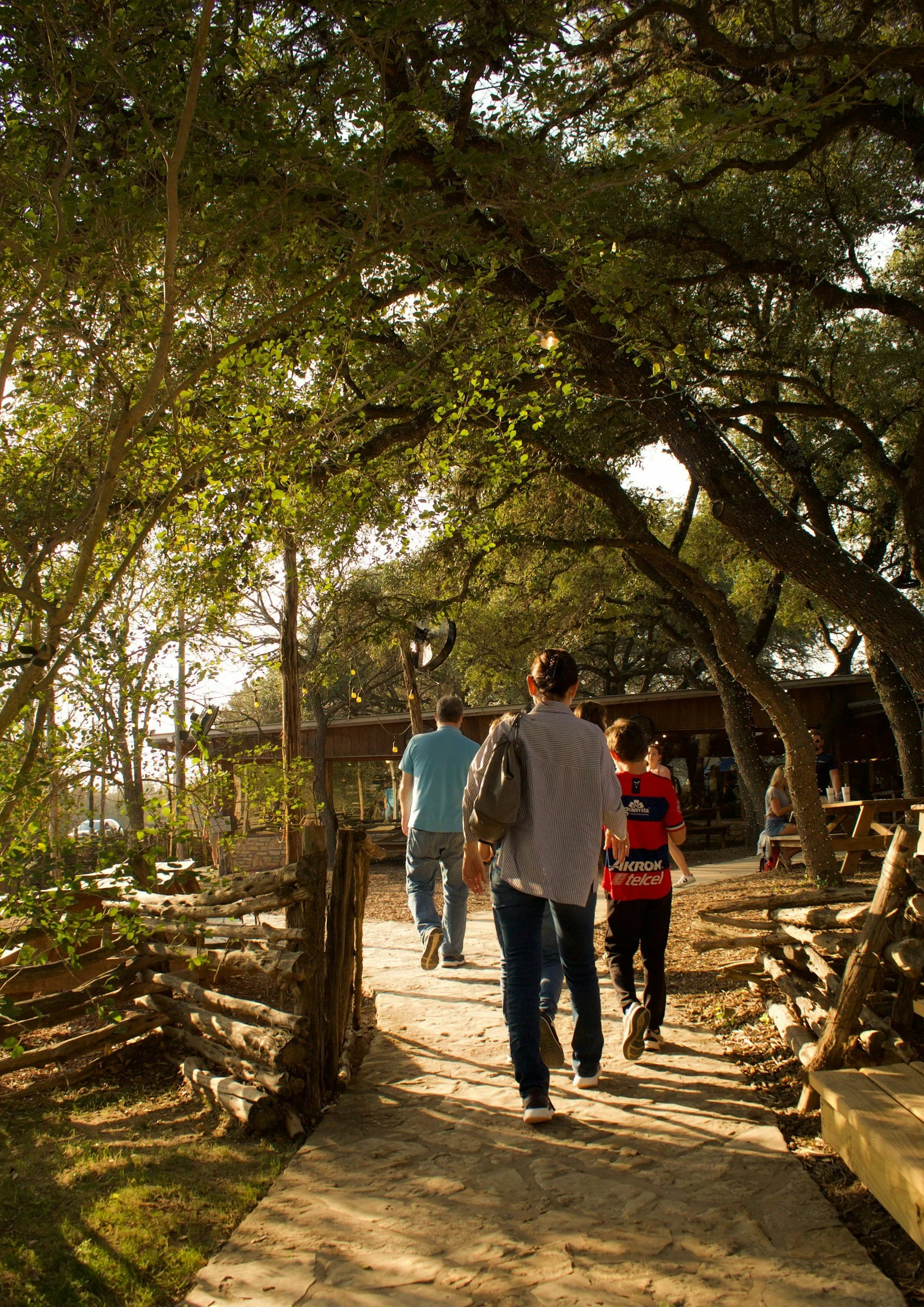 People walking on a stone path under trees in a park-like setting.