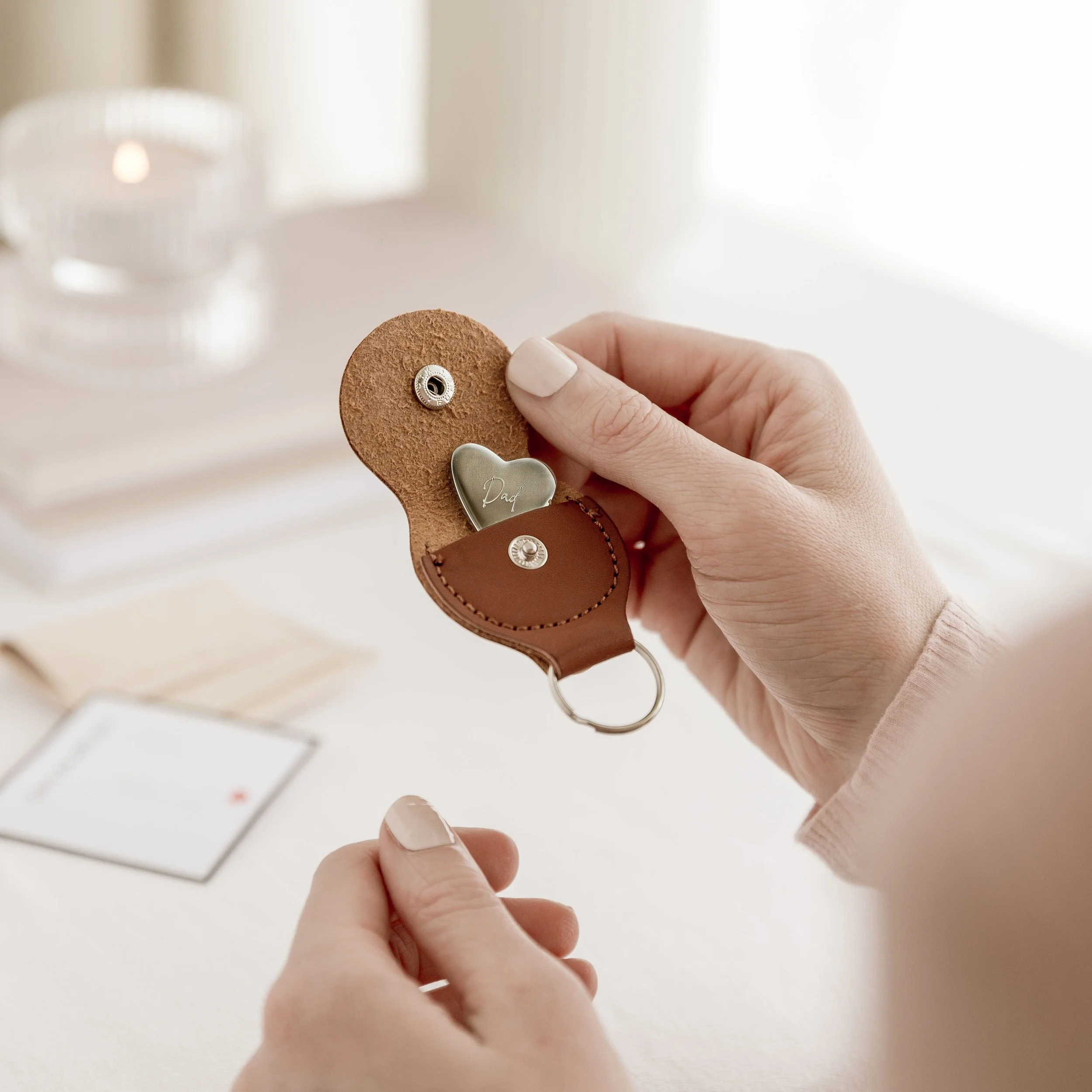 Close-up of a hand holding a leather keychain with a photo holder, a silver heart-shaped charm with 'Dad' engraved, and a keyring.