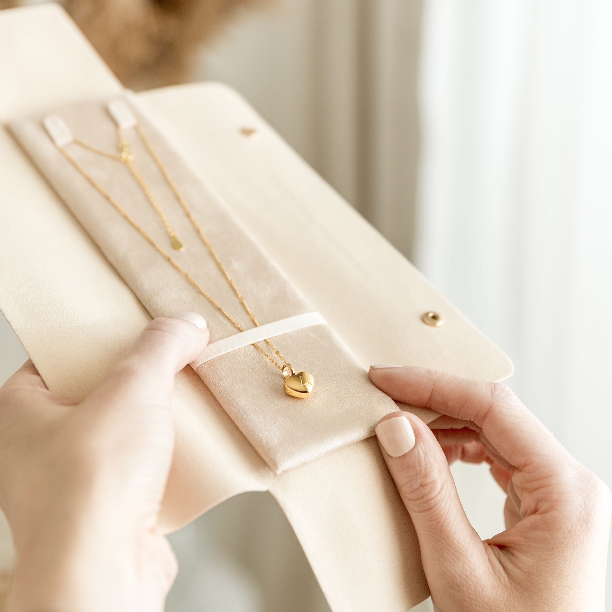 A person holding an open jewelry box with a gold heart-shaped necklace inside.