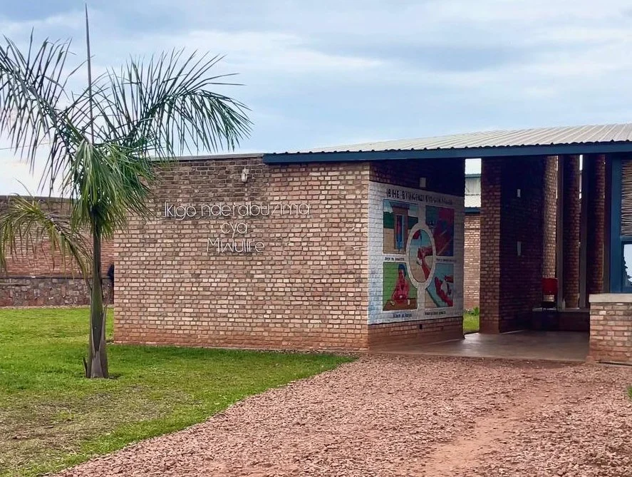 A brick building with an open portal and a groomed stone path leading up to it. A tree and green grass are in the foreground