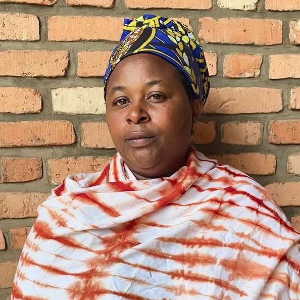 A woman with dark skin tone wearing a blue and yellow head scarf and an orange and white outfit