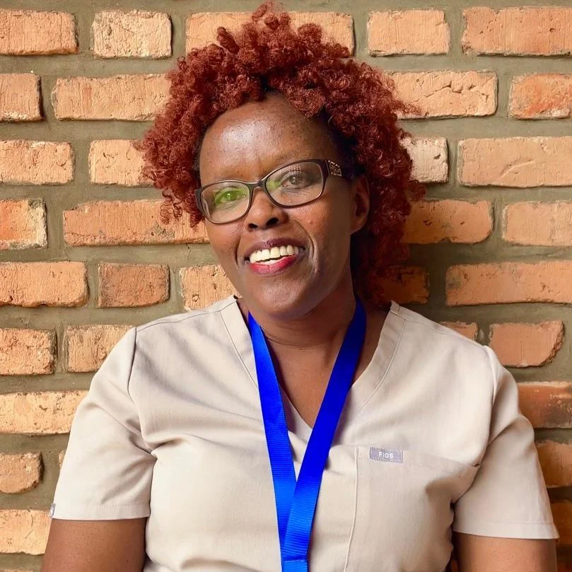 A smiling woman with dark skin tone and red hair curls wearing a light pink shirt and a blue lanyard